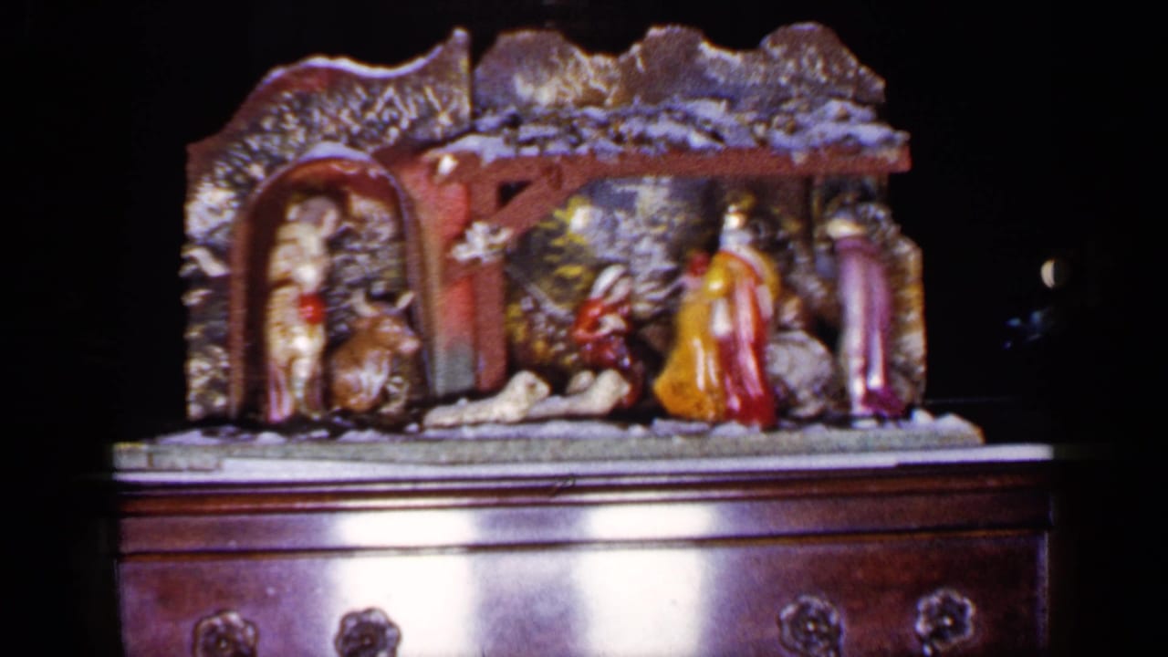 Tabletop nativity scene on a dark wooden chest, shown in a 1960s home-movie frame.