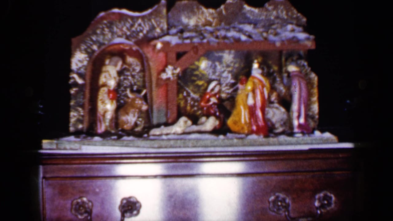 Nativity set with painted figures and animal shapes on a wooden chest against a dark background.