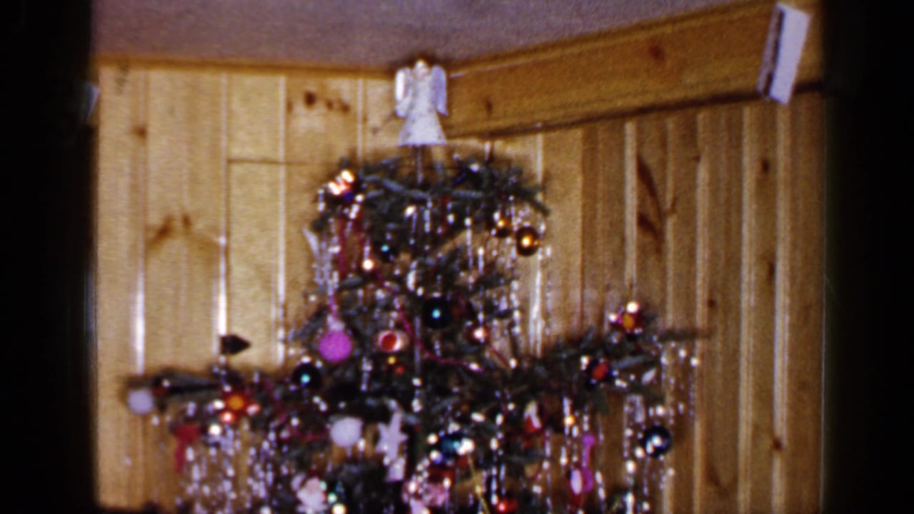 1965 Long Island home-movie frame showing a tall decorated Christmas tree with silver tinsel, ornaments, and an angel topper.