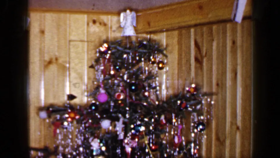 A Long Island 1965 holiday interior frames a decorated Christmas tree with dense tinsel and colorful ornaments.