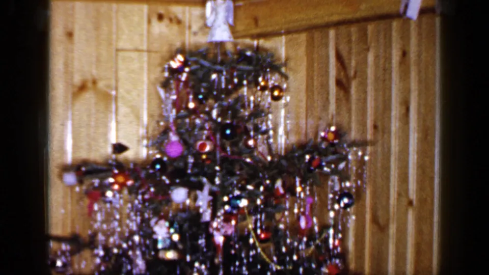 1965 home-movie still showing a decorated Christmas tree in a wood-paneled Long Island interior, with soft 8mm focus.