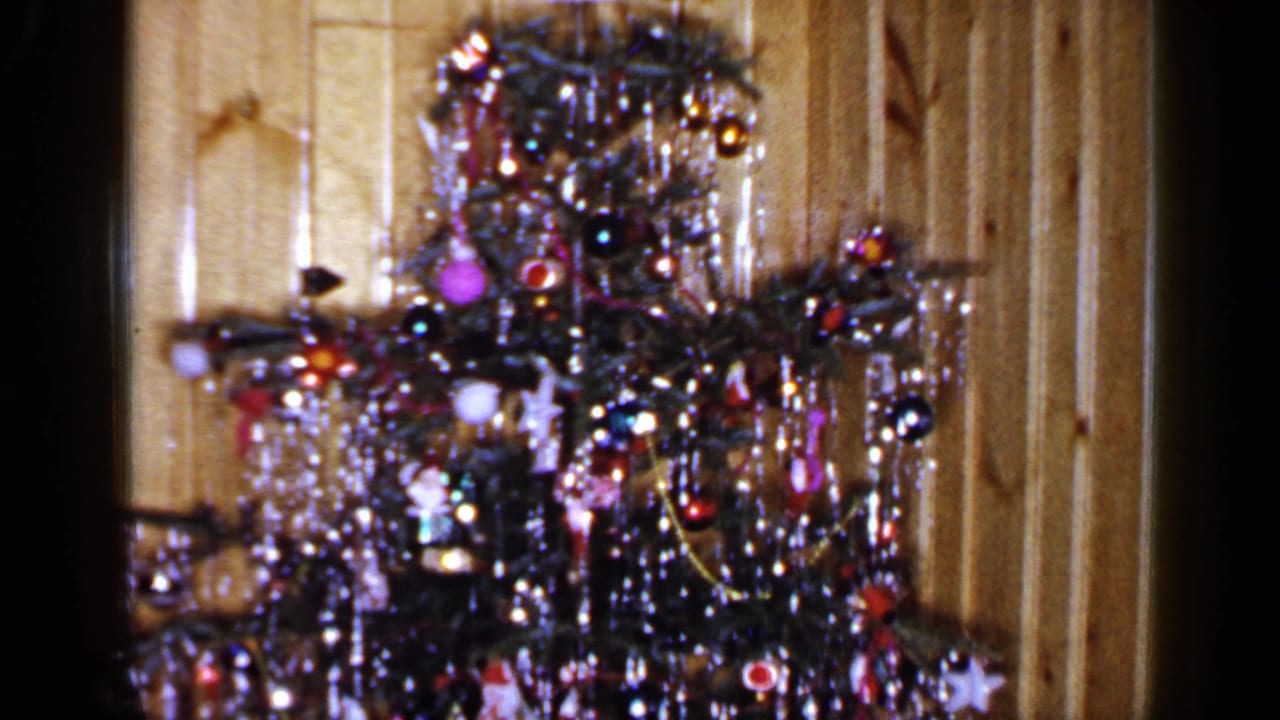 Decorated Christmas tree with tinsel and ornaments beside a wood-paneled wall.