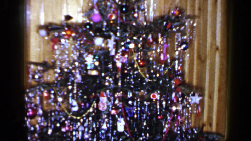 1965 Long Island home-movie frame showing the camera pan lower across the decorated tree and wood-paneled interior wall.