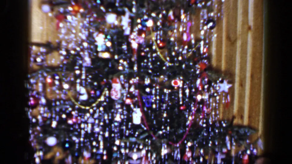 1965 Long Island home-movie frame ending on a dense section of the Christmas tree with ornaments, tinsel, lights, and garlands.