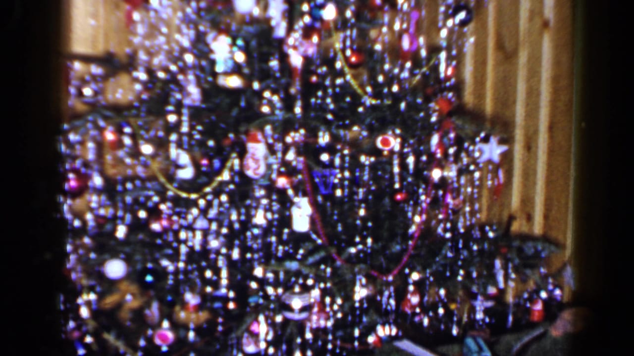Close view of a tinsel-covered Christmas tree with colorful ornaments and warm lights.