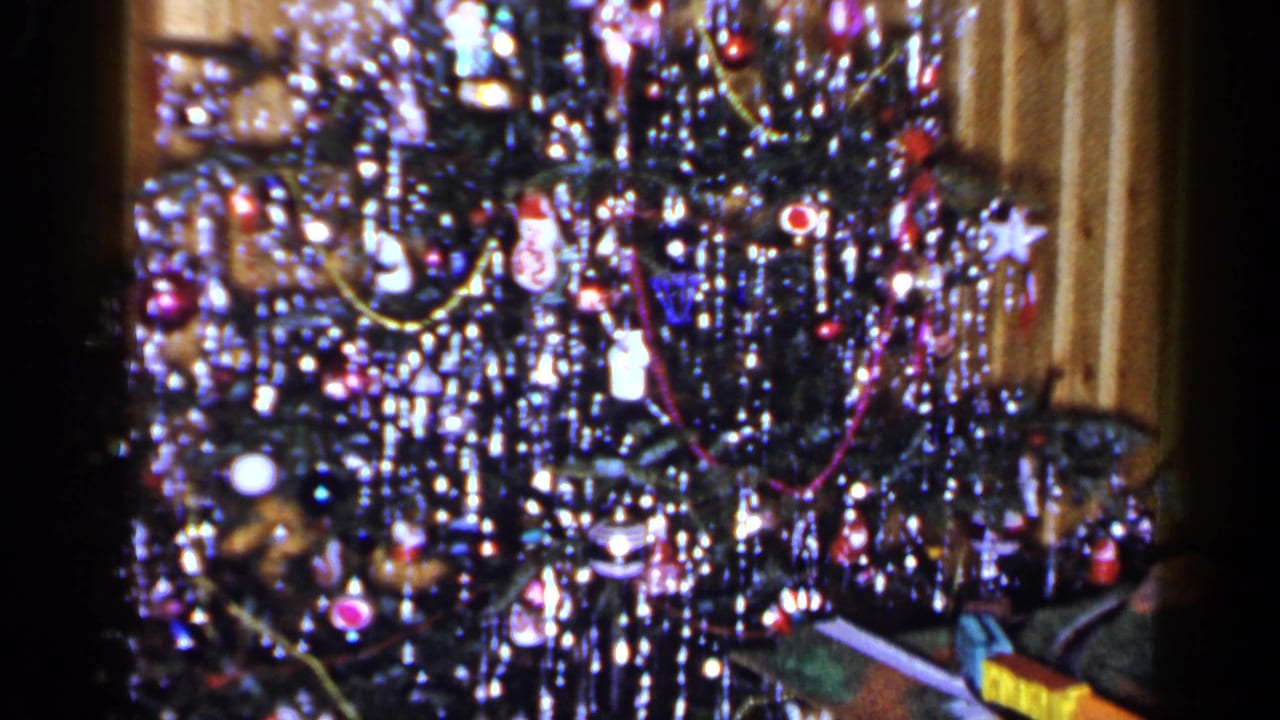 Decorated Christmas tree with tinsel, ornaments, and part of a toy train at the lower right.