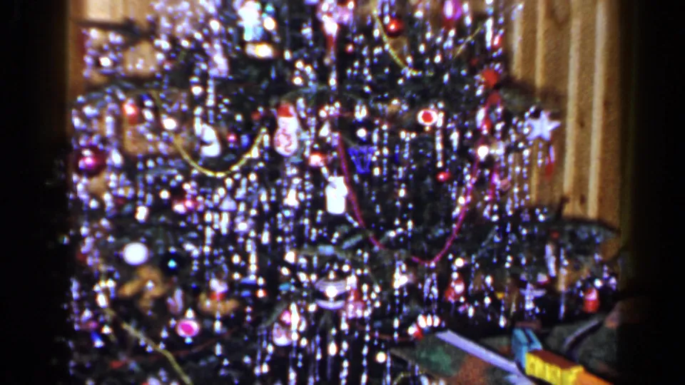 1965 Long Island frame of a tinsel-decorated Christmas tree with a toy train partly visible near the base.