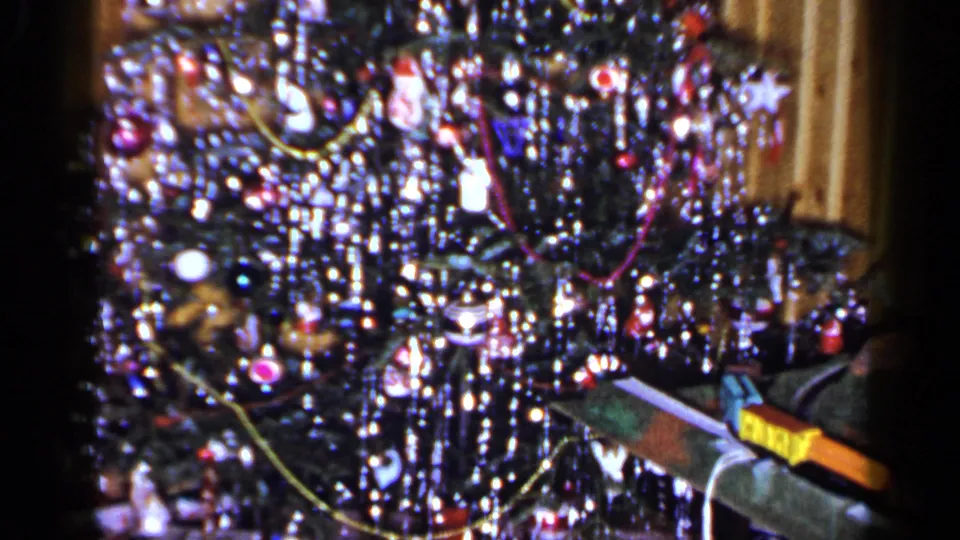 1965 Long Island home-movie still showing a tinsel-filled Christmas tree and toy train detail in the foreground.