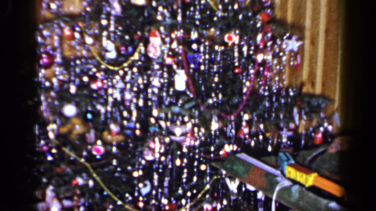 Tinsel-covered Christmas tree with ornaments, lights, and wrapped packages partly visible at the lower edge.