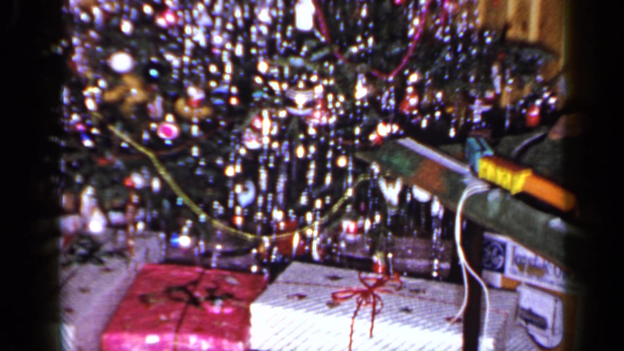 1965 Long Island 8mm frame showing wrapped presents beneath a tinsel-covered Christmas tree, including pink and white packages with red ribbon.