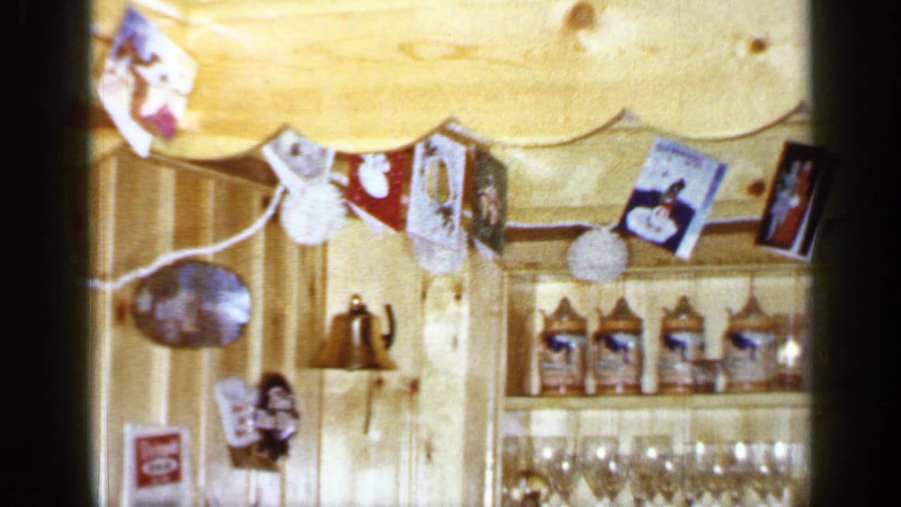 A 1965 Long Island home interior shows holiday cards, a hanging bell, shelves of glassware, and kitchen or dining canisters.