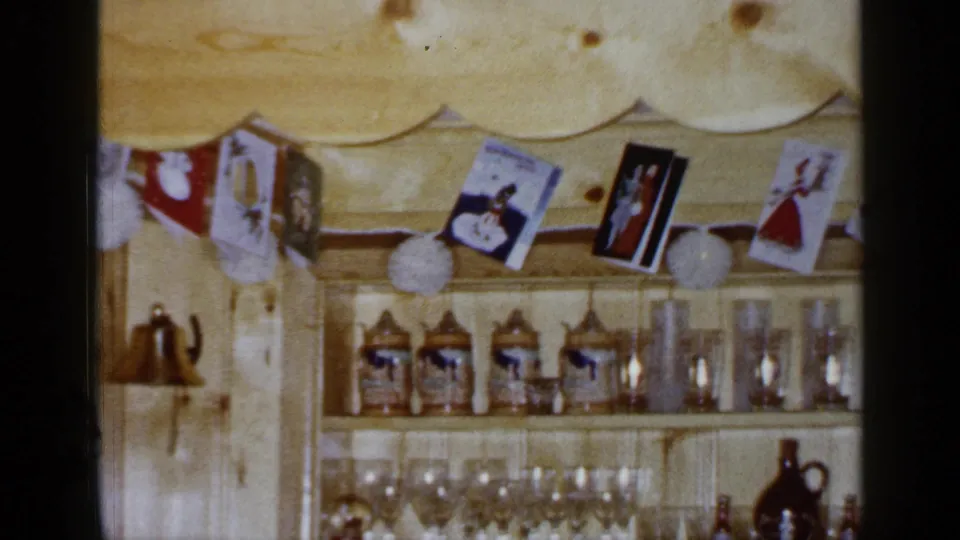 1965 Long Island pine-paneled room showing open shelves with steins, glassware, hanging cards, and white paper decorations.