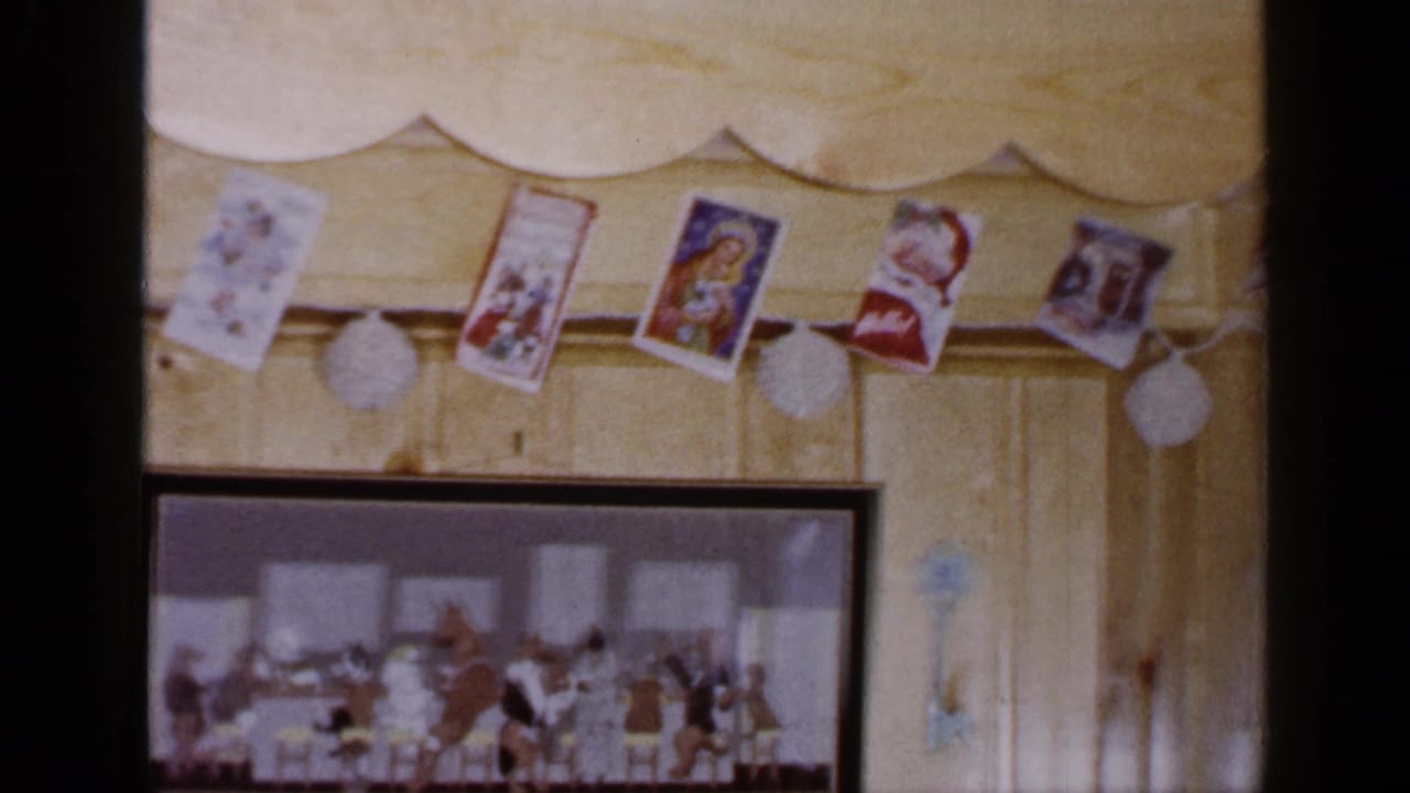 Mid-pan view of a 1965 Long Island Christmas wall display with paper cards, white pom-poms, and a framed holiday illustration.