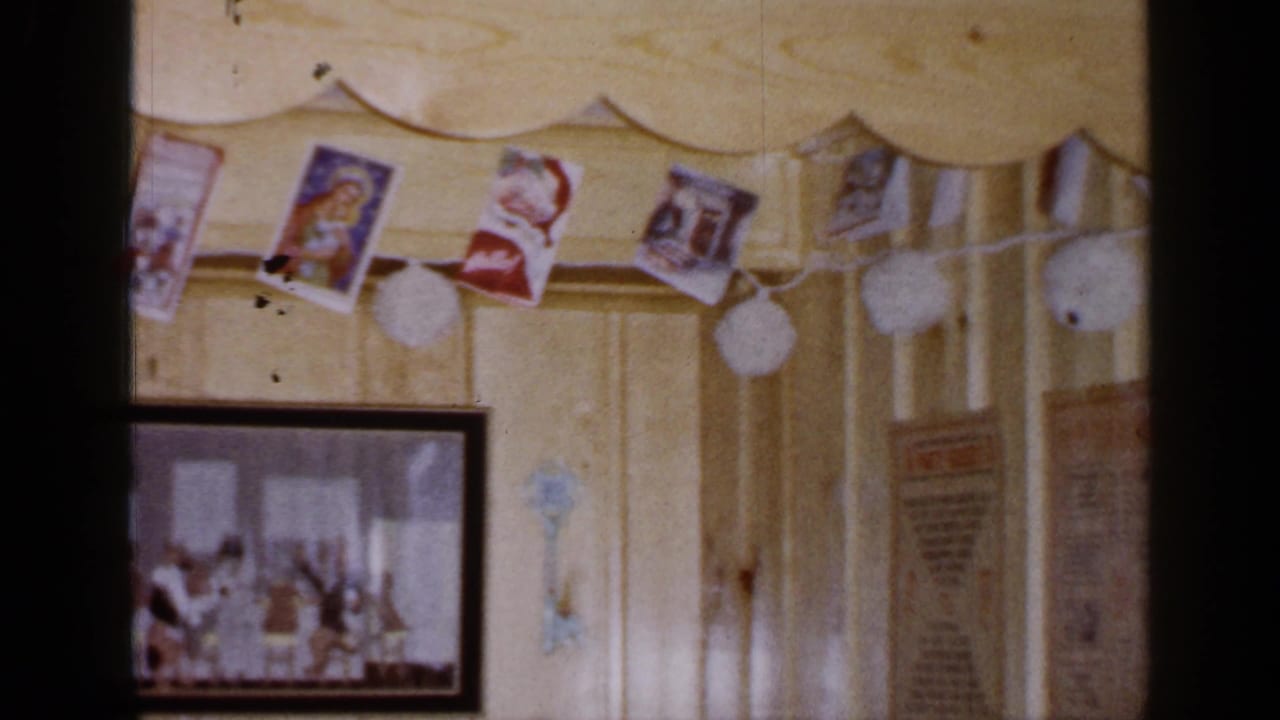 1965 Long Island interior detail with Christmas cards and pom-pom garland above a partially visible framed picture and wall papers.