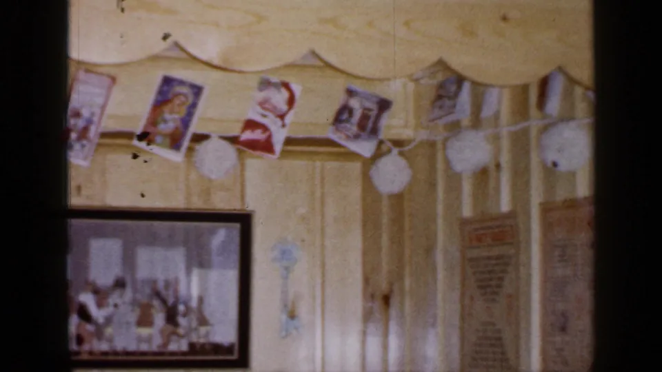 1965 Long Island interior detail with Christmas cards and pom-pom garland above a partially visible framed picture and wall papers.