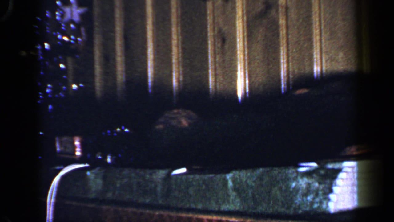 Toy train display in a dim room with wood paneling and a Christmas tree edge.