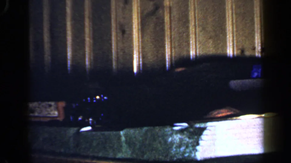 A dim 1965 indoor frame shows part of a toy train layout against vertical wood paneling, with small lights and miniature scenery visible.