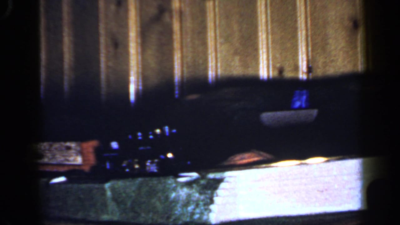The 8mm frame shows the toy train layout from another moment, with miniature details, a bright wall section, and a dark room interior.
