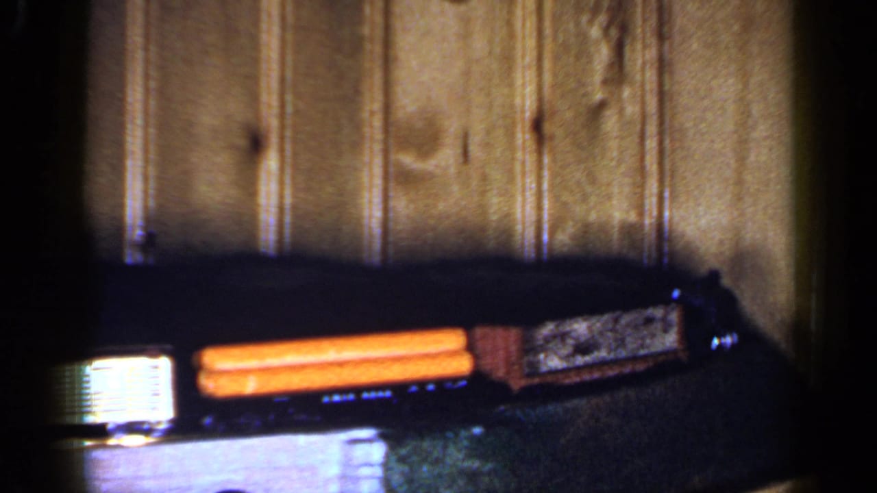 Small toy train cars on a dark track beside a wood-paneled wall.
