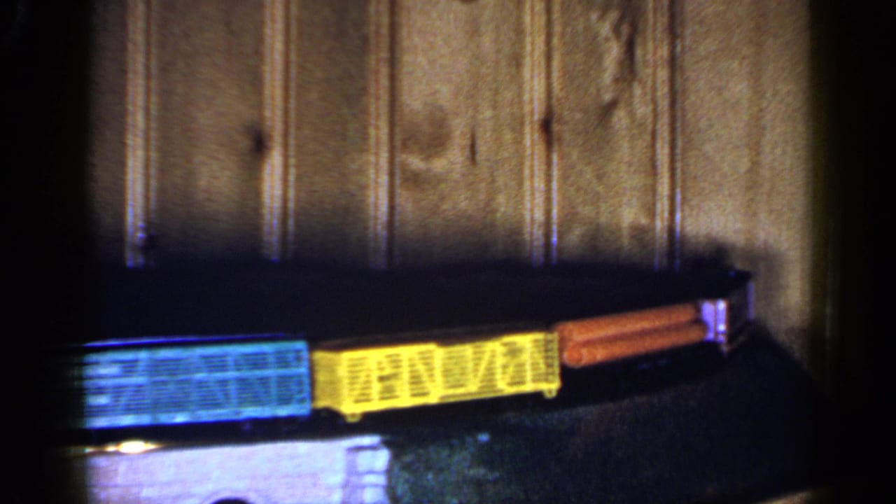 Blue, yellow, and orange toy train cars moving across a dark surface.