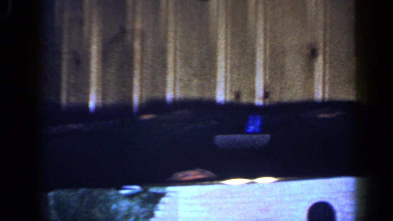 Dark toy train cars pass through a soft 8mm frame, with curved track and wood paneling visible behind them.