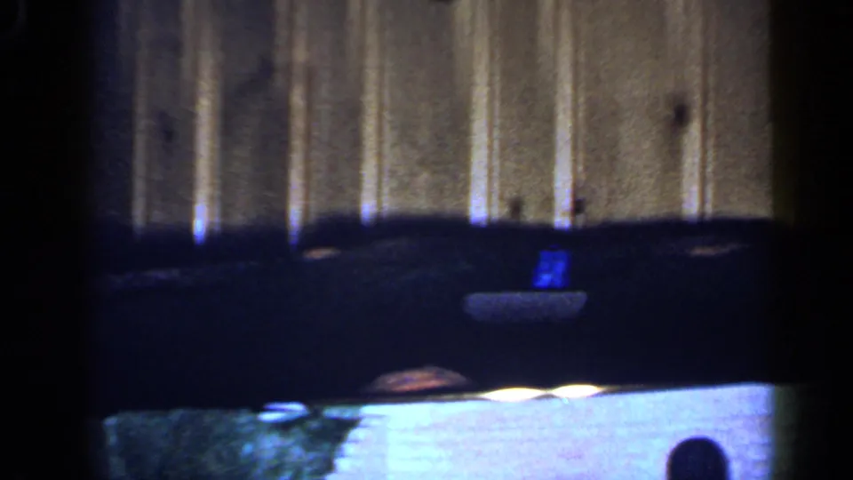 Dark toy train cars pass through a soft 8mm frame, with curved track and wood paneling visible behind them.