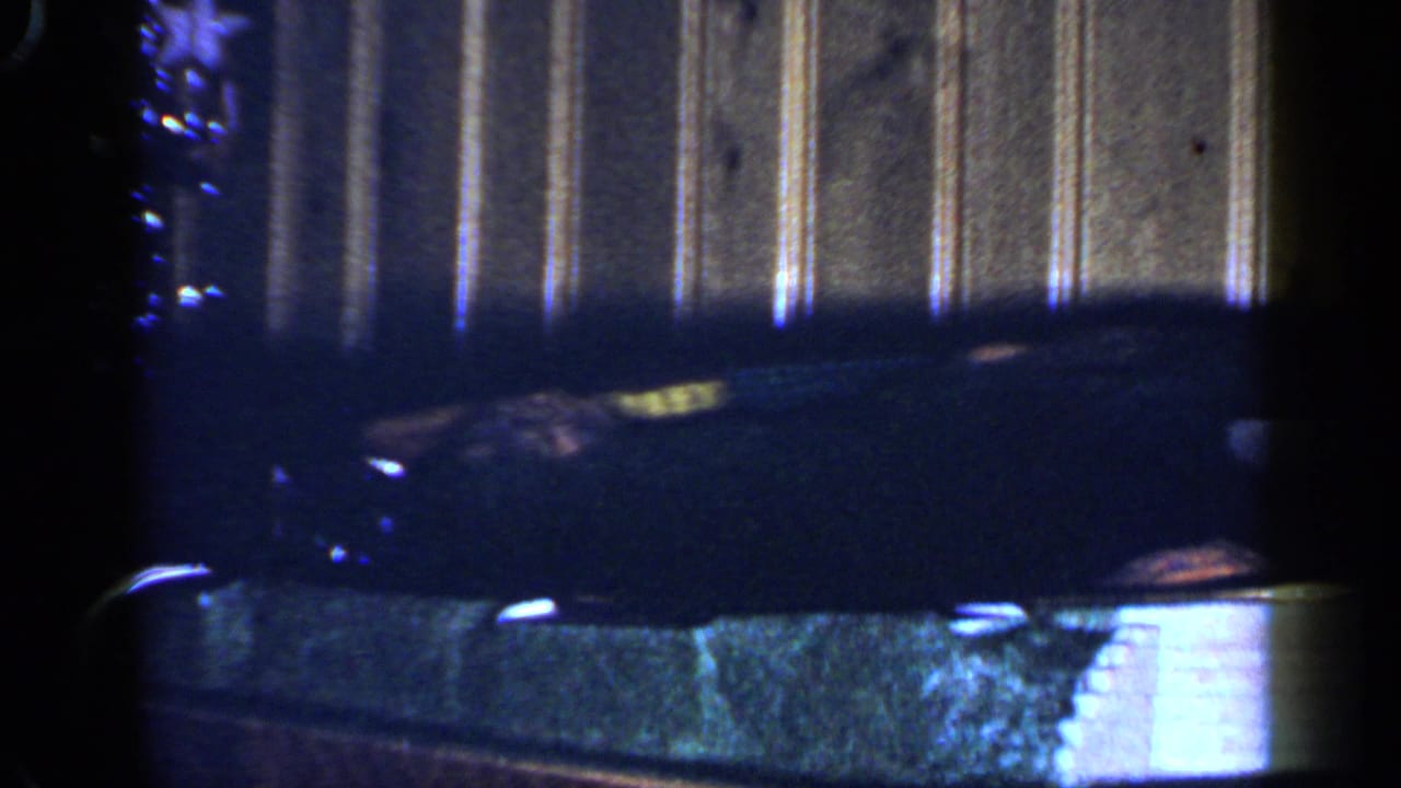 A dark toy engine appears close to the camera as the train rounds the indoor track in this 1965 home-movie frame.