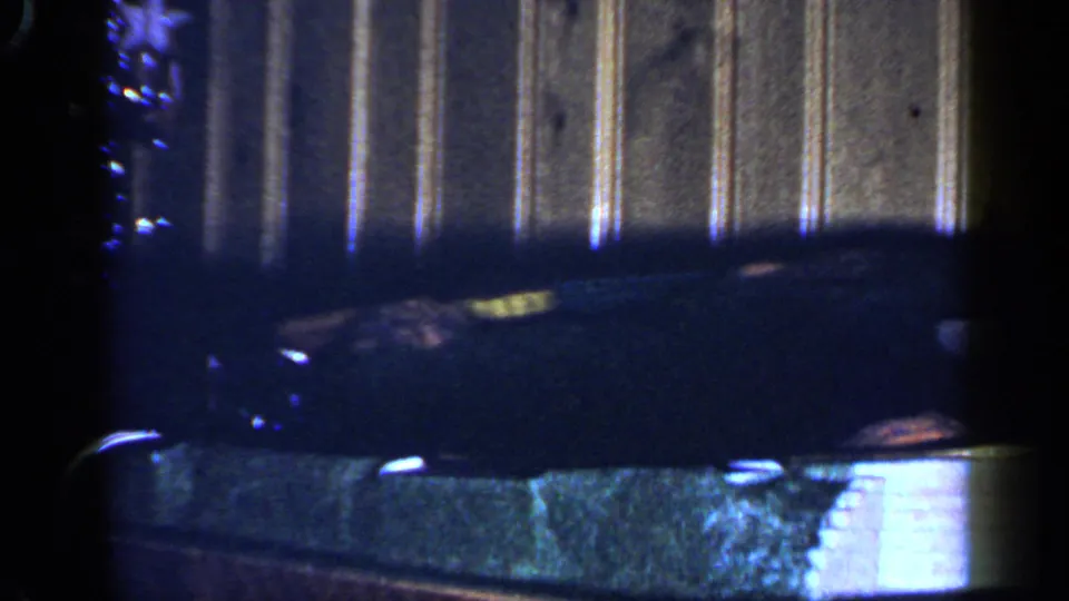 A dark toy engine appears close to the camera as the train rounds the indoor track in this 1965 home-movie frame.