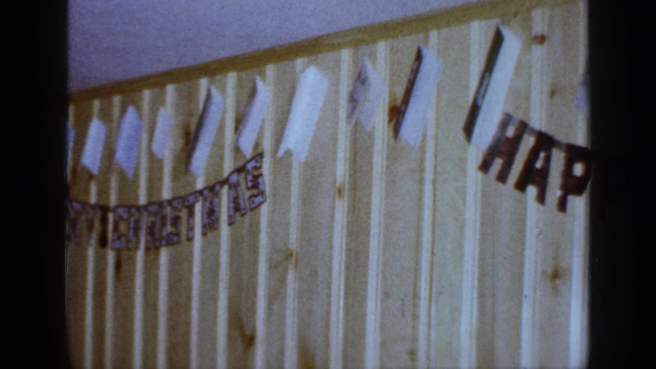 1965 Long Island 8mm frame showing the right side of a HAPPY BIRTHDAY banner and paper decorations on a paneled wall.