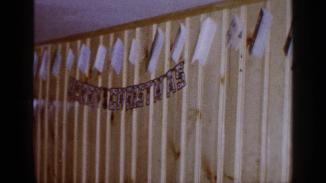 Closer pan across the MERRY CHRISTMAS banner and taped paper shapes on paneled wall.