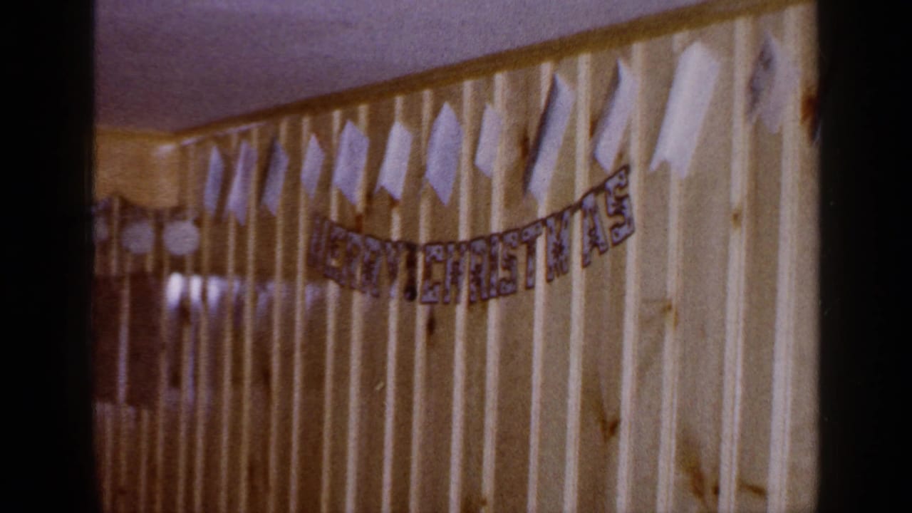 A home-movie pan shows the Christmas banner crossing pale paneling, with darker wood paneling and reflective highlights at left.