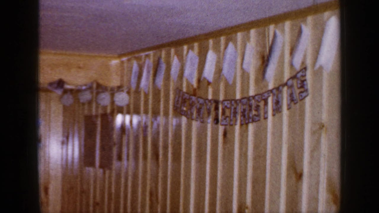 Final 1965 Long Island frame shows the banner stretched across pale wood paneling, with adjacent darker interior wall detail visible.
