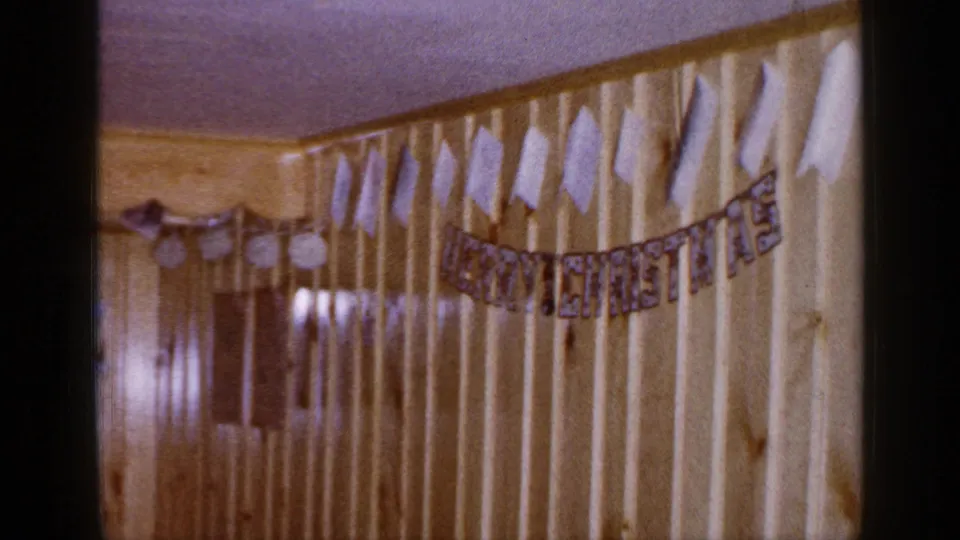 Final 1965 Long Island frame shows the banner stretched across pale wood paneling, with adjacent darker interior wall detail visible.