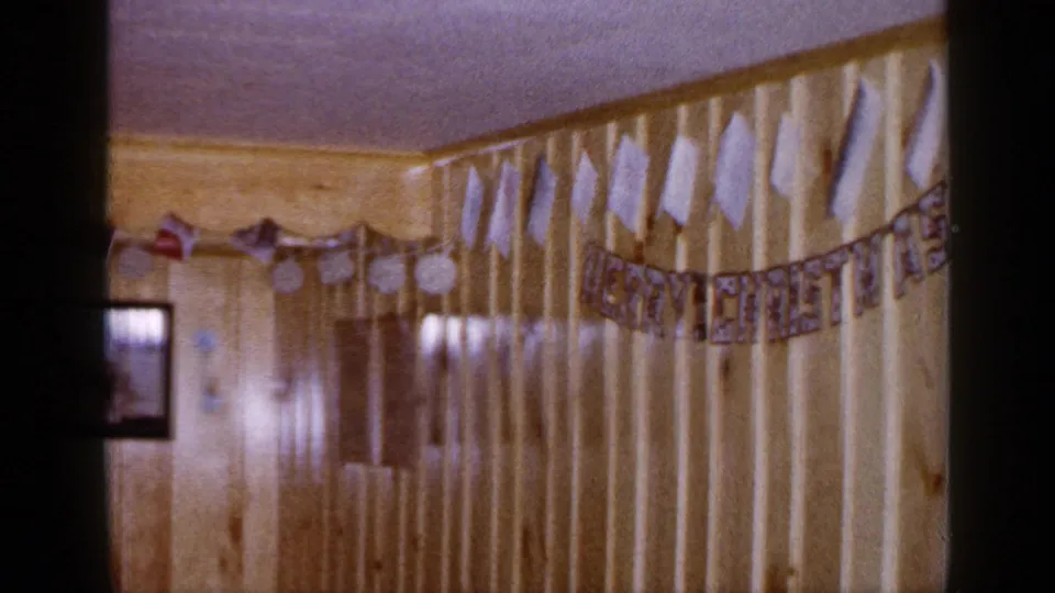 1965 Long Island home interior with wood paneling, handmade holiday decorations, small flags, and a framed family photograph on the wall.