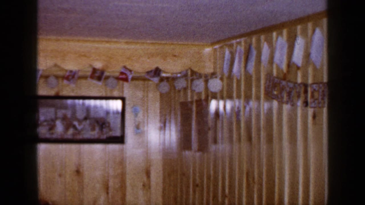 Wood-paneled Long Island room decorated for Christmas, with paper garland, flags, and a framed family photograph visible on the wall.