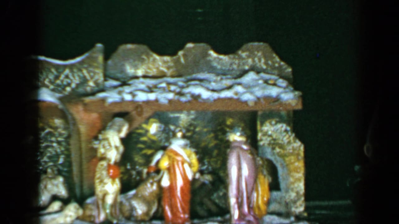 1965 Long Island home-movie frame showing a Christmas nativity set with figures arranged inside a small rustic stable.