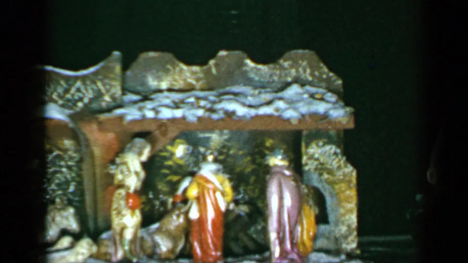 1965 Long Island home-movie frame showing a Christmas nativity set with figures arranged inside a small rustic stable.