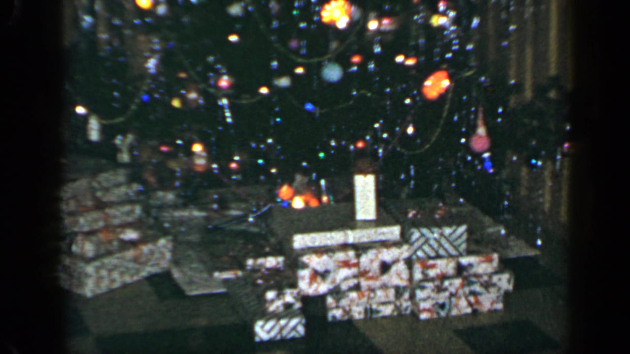 Home-movie view of wrapped Christmas presents under a lit and ornamented tree in a Long Island interior, 1965.