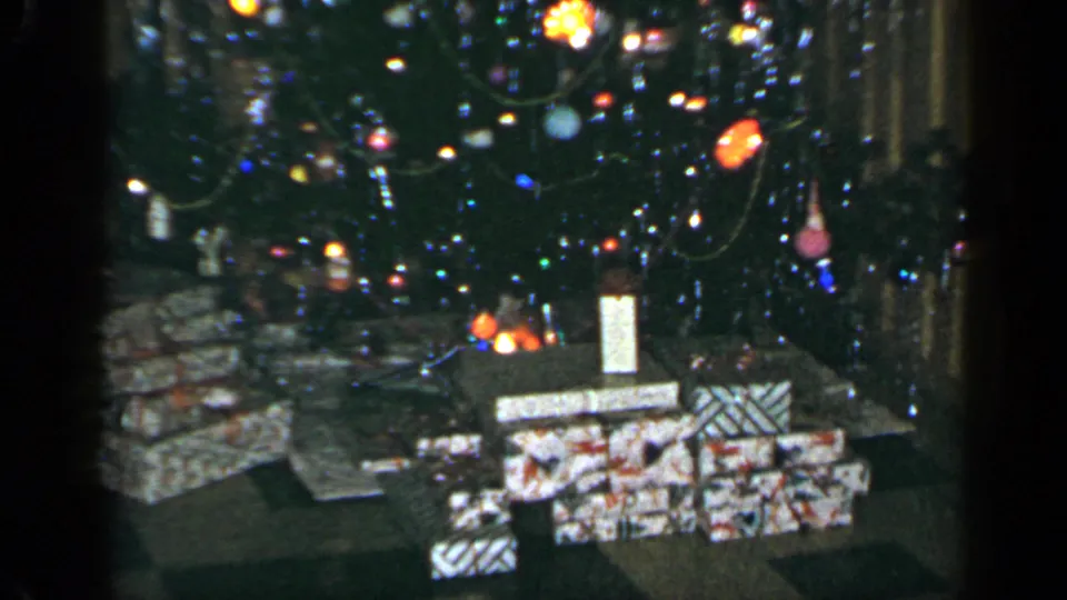 Home-movie view of wrapped Christmas presents under a lit and ornamented tree in a Long Island interior, 1965.