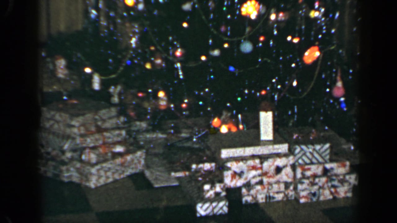 1965 Long Island holiday interior with a lit Christmas tree, hanging ornaments, and wrapped presents arranged below.