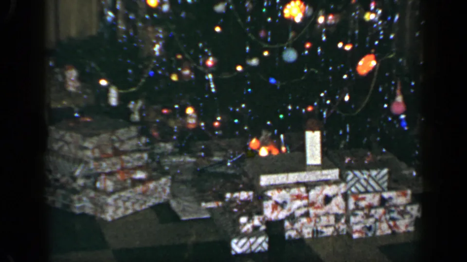 1965 Long Island holiday interior with a lit Christmas tree, hanging ornaments, and wrapped presents arranged below.
