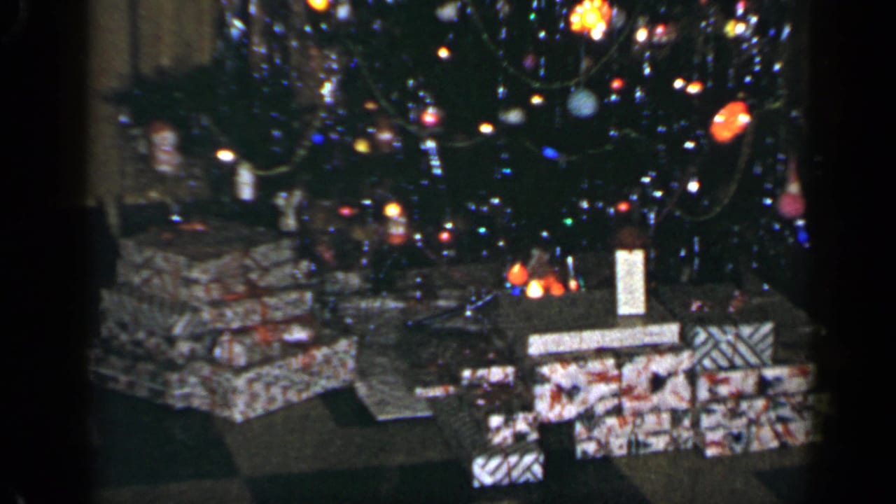 Decorated Christmas tree with wrapped presents underneath in a dim interior.
