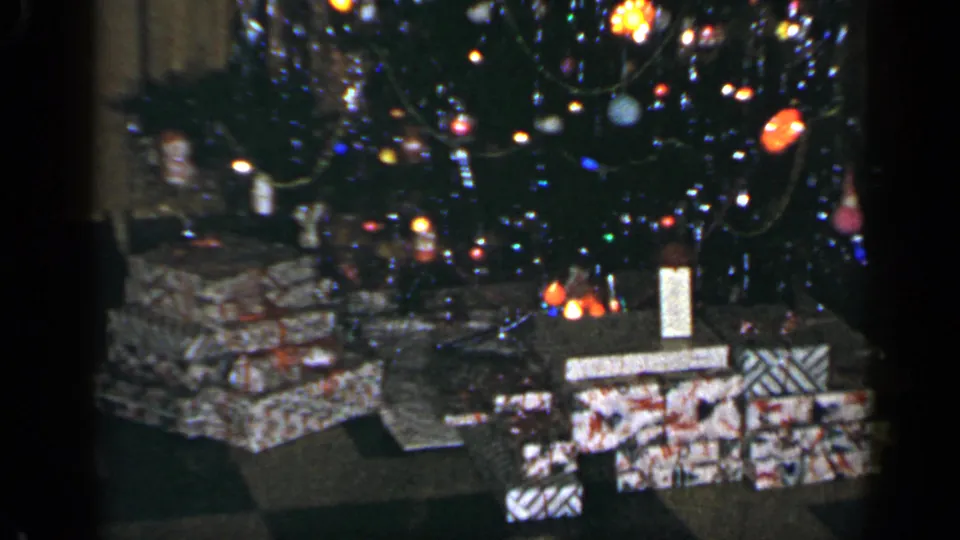 1965 Long Island 8mm frame showing a lit Christmas tree with ornaments, tinsel, and wrapped presents below.