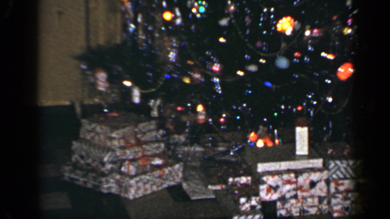 1965 Long Island home-movie frame of wrapped gifts arranged below a decorated Christmas tree in an interior room.