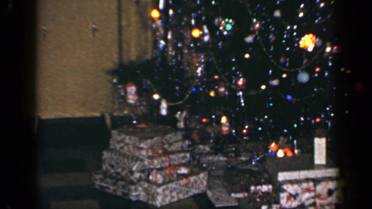 1965 Long Island 8mm frame with stacked wrapped presents, a decorated tree, and warm colored lights in a family interior.