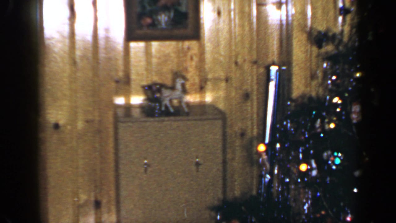 Wood-paneled room with a dresser, small objects, and part of a decorated Christmas tree.