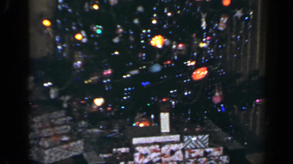 Close 8mm view of a 1965 Long Island Christmas tree with glowing lights, ornaments, tinsel, and gifts underneath.
