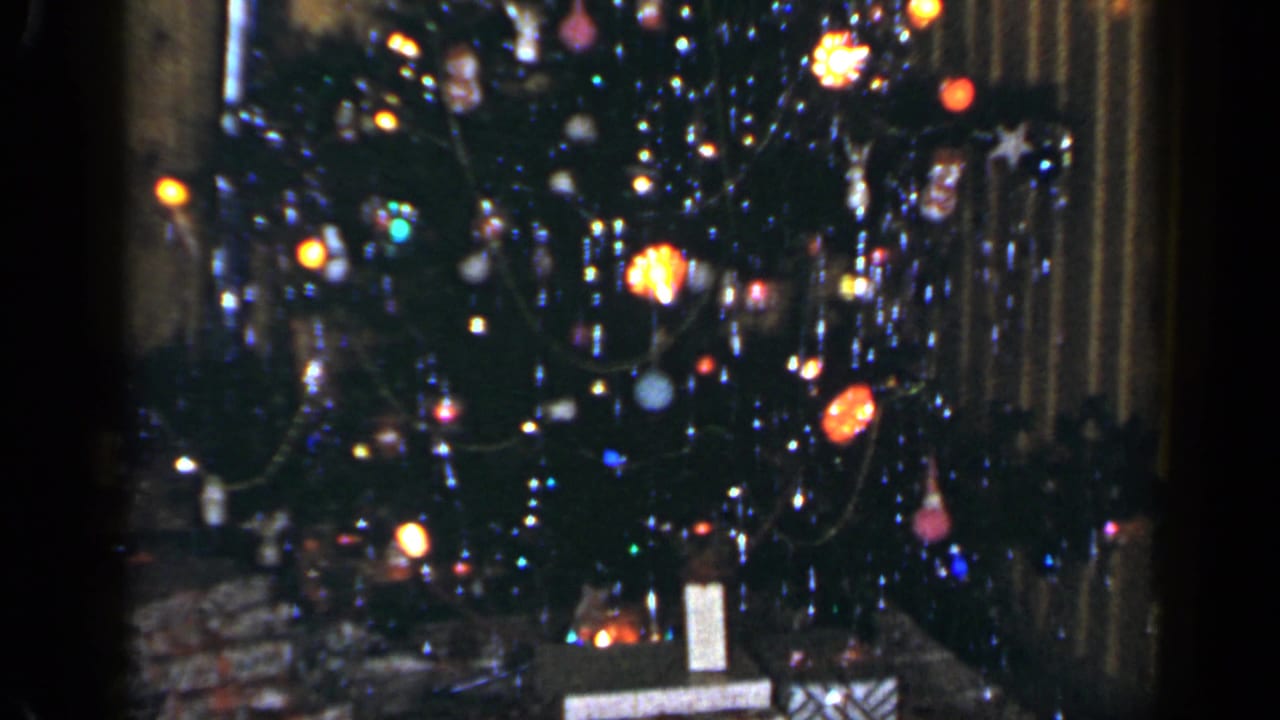 1965 Long Island holiday interior showing a lit Christmas tree with ornaments, tinsel, and presents against wood paneling.