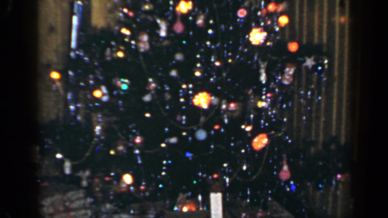 1965 Long Island home-movie frame showing a lit decorated Christmas tree in a wood-paneled interior.