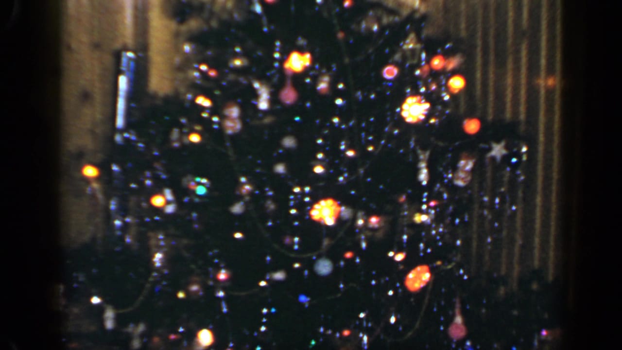Decorated Christmas tree with colored lights and ornaments in a dim interior.